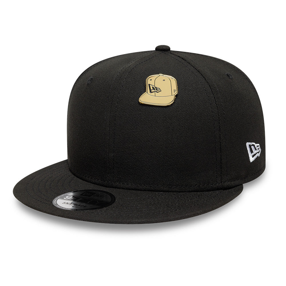 Guld New Era NE Cap Badge, lille taskeaccessory, synlig i billedet med tydeligt logo og detaljer.