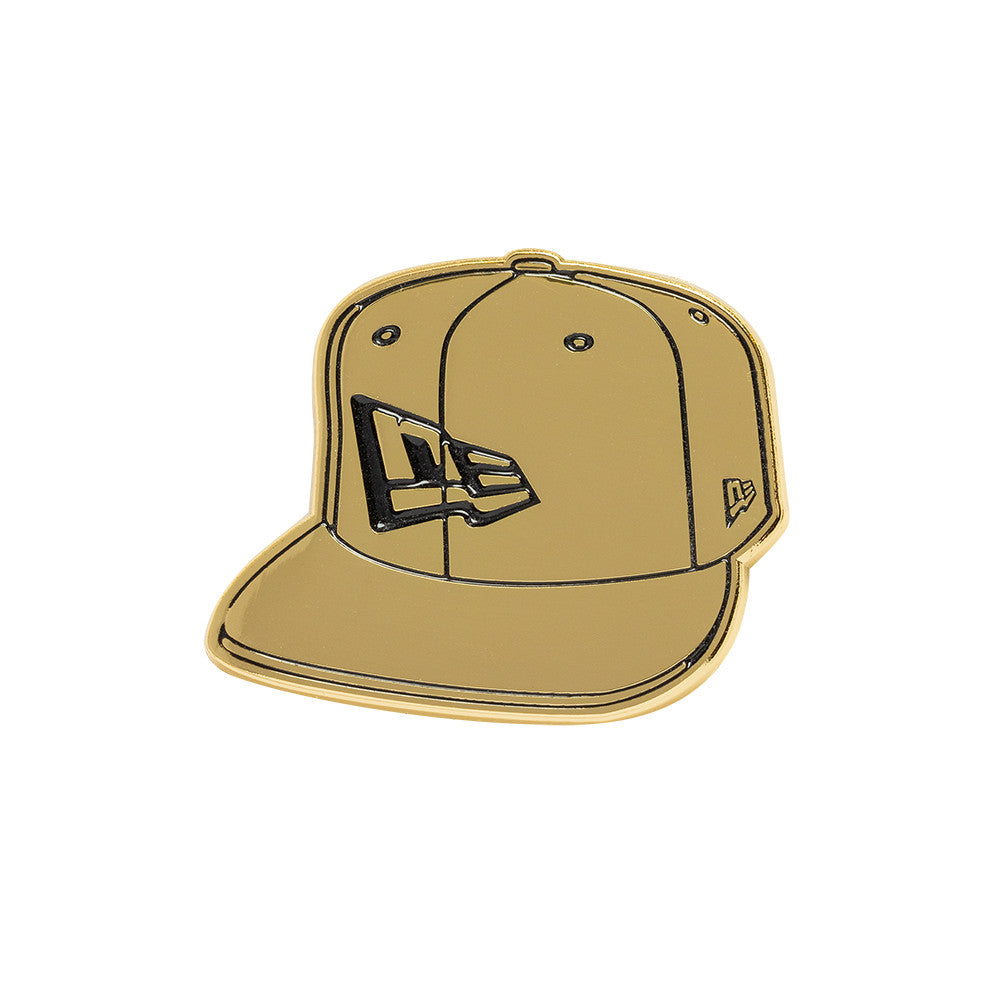 Guld New Era NE Cap Badge på en taske, lille, rund metalpresse med New Era-logo, dekorativt tilbehør.
