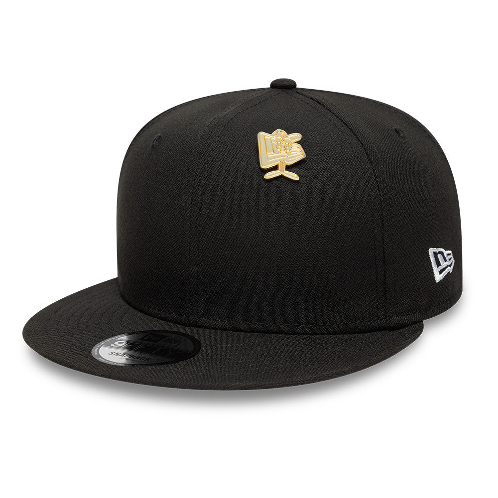 Guld New Era NE Cap Flag Badge fastgjort til en taske, detaljeret og skinnende metalbadge.