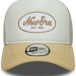 Beige og hvid trucker cap med oval skumpatch fra New Era, afslappet og stilfuld hovedbeklædning.