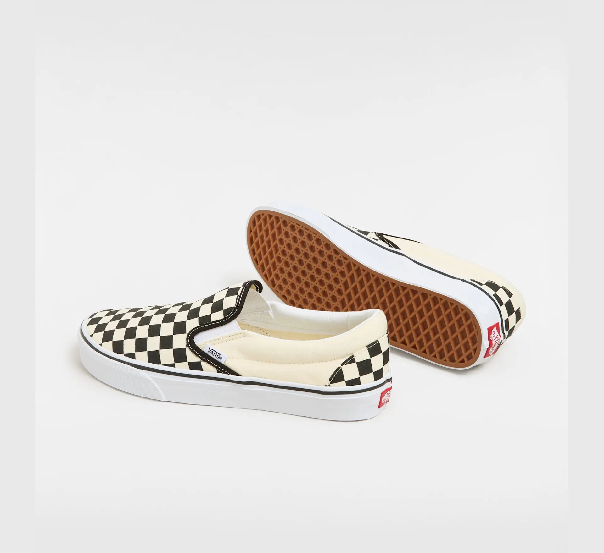 Sort og hvid checkerboard VANS Classic Slip-On sko med lav profil og elastiske sider, vist på en model.
