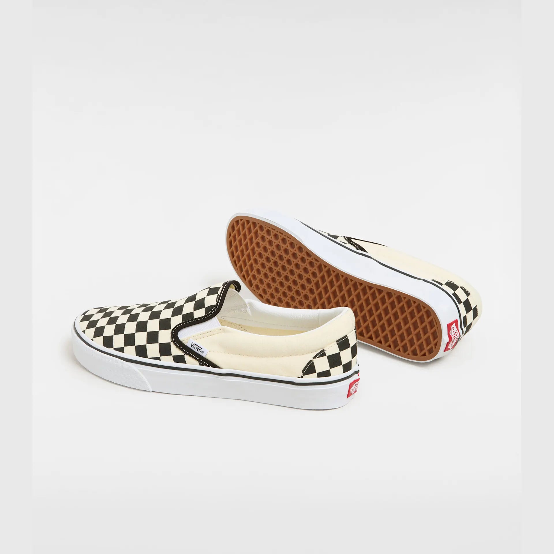 Sort og hvid checkerboard VANS Classic Slip-On sko med lav profil og elastiske sider, vist på en model.