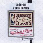 Hvid Mitchell & Ness Vince Carter 1998 SWINGMAN basketballtrøje, vises på model med detaljeret fokus på jerseyens design.